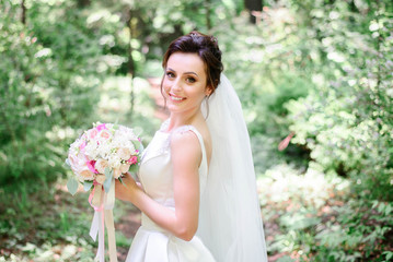 happy and young bride in white dress standing outdoors