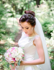 happy and young bride in white dress standing outdoors