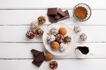 Homemade chocolate and nuts candy balls with cocoa powder, coconut, berries and chopped hazelnuts on white wooden background, top view. Healthy Eating concept