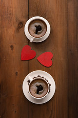 Two cups of hot coffee and red wooden hearts on rustic dark textured background. Valentine's day celebration concept, top view
