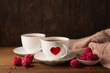 Two cups of hot tea and strawberry chocolate candies on rustic dark wooden background. Valentine's day celebration concept