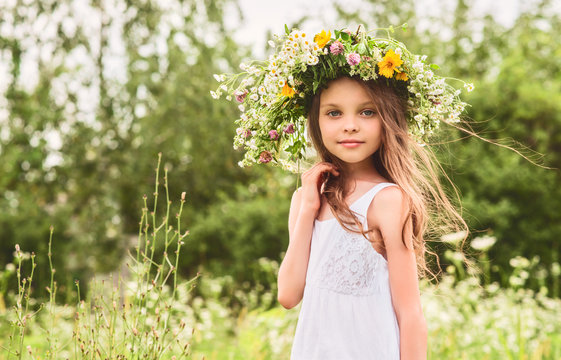 Cute smiling little girl  with flower wreath on the meadow at th