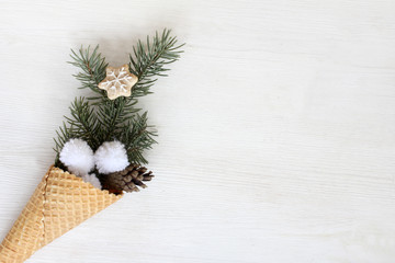 winter ice cream for the holiday/ waffle cone with fir branch, pine cones and ginger cookies on a light wooden surface 