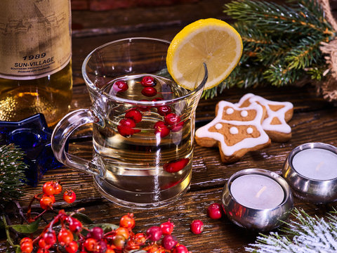 Warming tea with berries and alcohol. Christmas still life with mug decoration lemon slice hot drink and bottle white wine. Bottle has label.
