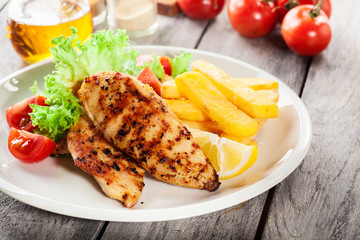 Grilled chicken breasts served with fries and fresh salad