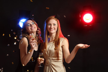 Two cheerful women with glasses of champagne in his hand, having fun at a party.