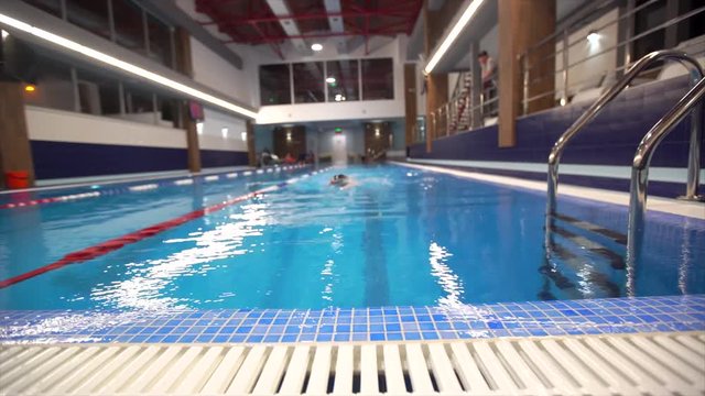 Girl child swimmer in a red bathing suit on a background of the pool inside the room with glasses and a cap.