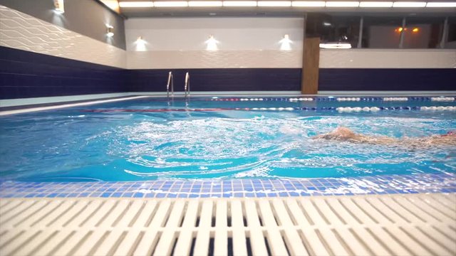 Girl child swimmer in a red bathing suit on a background of the pool inside the room with glasses and a cap.
