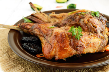 Roasted rabbit leg with prunes on a ceramic plate on light background. Close up. Holiday menu. Easter, Christmas.
