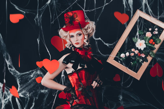 Queen of Hearts entered into the real world. Photo shoot in the style of the card game. Unusual, creative make-up, beautiful, funny dress. Vintage hairstyle. Studio photography, fashionable toning