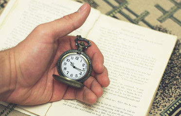 Old pocket watch in the hand on the background of the book