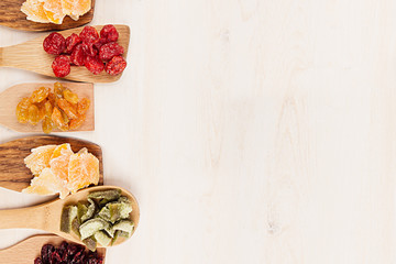 Assortment of dried fruits on wooden spoons on white background. Decorative border of dry exotic fruit. Top view.