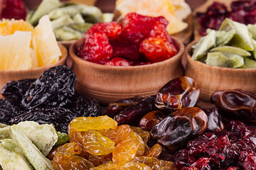 Assortment of dried fruits closeup on brown wooden background. Decorative border of dry exotic fruit in spoons, bowl.