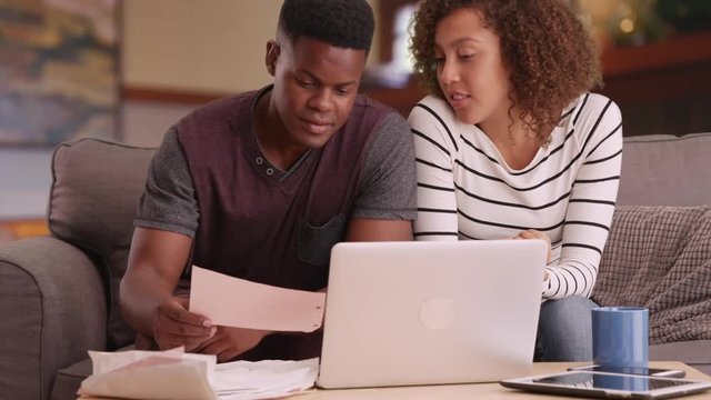 Black millennial couple paying bills with laptop computer in living room