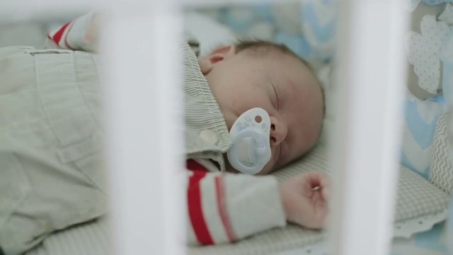 An infant boy falling asleep in his cradle.