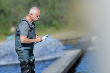 old worker at a fish farm writing down data