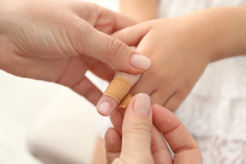 Woman wrapping sticking plaster around little girl's finger, close up view