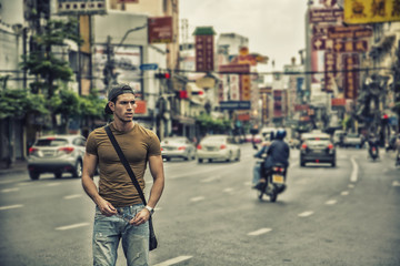 Muscular young handsome man walking on busy sunny street in Bangkok, Thailand.