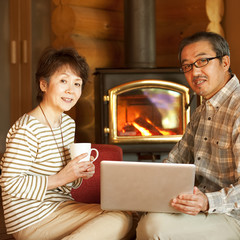 暖炉の前でパソコンをするシニア夫婦