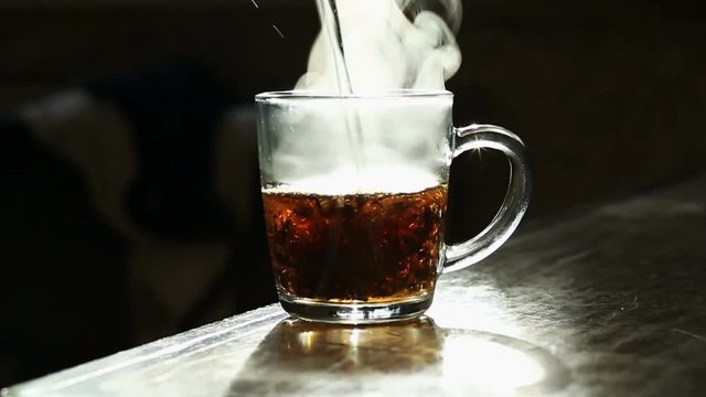 Close up of woman pouring hot water over tea bag in transparent glass cup 