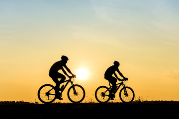Fototapeta na wymiar Silhouette of cyclist with friend motion on sunset background