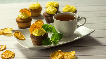 Tasty cupcakes with caramelized orange, mint and cup of tea close-up