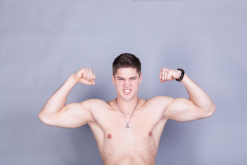 young man with relief muscles in jeans with a naked torso on a gray background