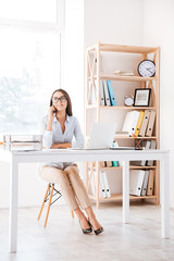 Businesswoman sitting in her office and talking by phone