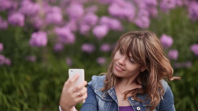 A young girl takes pictures on your phone, selfi among the flowers.