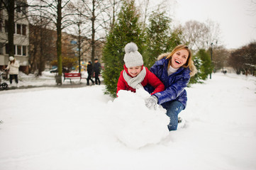 Mother with daughter of younger school age build a snowman in the yard.