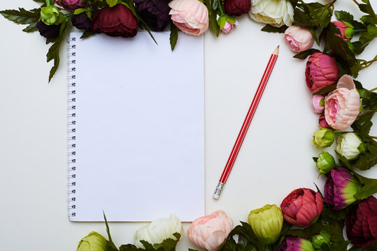 Jotter and red pencil circled by colorful flowers