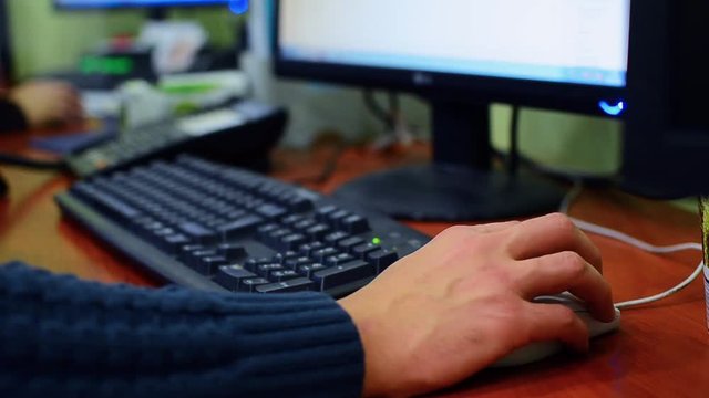 man,sit in the armchair, talking on the phone. On a computer screen he view financial information. Closeup. Shallow depth of field