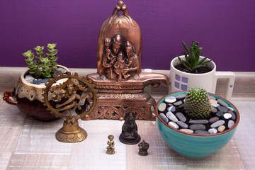 statues of Hindu gods and succulents in ceramic pots on purple background wall
