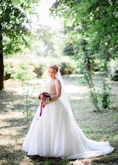happy and young bride in white dress standing outdoors