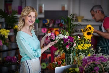 Fotobehang Bloemenwinkel Glimlachende bloemist die water op bloemen in bloemenwinkel sproeit