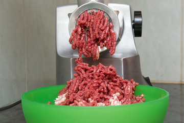 Electric meat grinder grind a meat. Minced meat falling in the bowl. Cooking at home in the kitchen. Healthy eating and lifestyle.