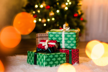 Some nice presents in a new year wrapping paper on a furry white carpet, beautiful christmas tree on the background. Christmastime celebration, home decorated with festive balls, copyspace