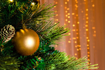 A close picture of a bright golden christmas toy hanging on a green tree, blurred warm background with golden tinsel. Decorated Christmas tree on lights background, copyspace.