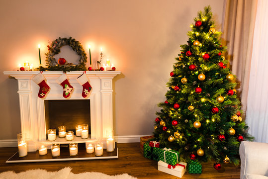 Wonderful new year details, beautiful furry tree with presents under it and a white fireplace full of candles. Xmas Home Interior Decoration, Hanging Sock and Present Toys.