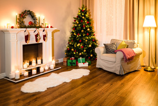 A cozy living room full of warm light from decorations for a coming Christmas, nice fireplace, soft sofa and a great tree. Room Christmas Tree Fireplace Light, Xmas Home Interior Decoration.
