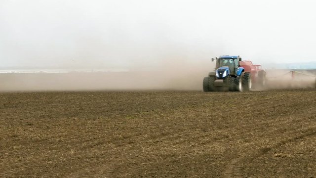 Field engine tractor seeder runs ploughs tills and plows on the field. Spring time planting seeding agricultural scene.