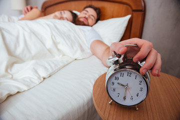 Couple sleeping in bed while man stretching hand to alarm