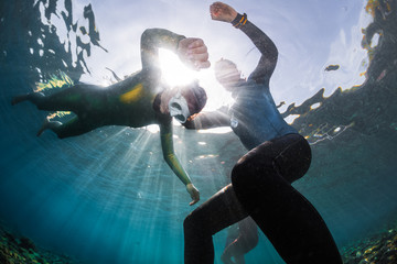 Underwater shot of the freedivers training static breath hold in shallow water of a calm bay. Coach watching student - obrazy, fototapety, plakaty