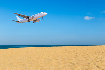 Fototapeta na wymiar passenger airplane landing above blue sea and tropical beach on blue sky background