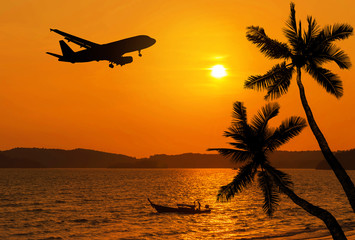 sunset on tropical beach and coconut palm tree and fisherman boat with silhouette airplane flying over the sea in thailand