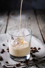 Pouring coffee liqueur in glasses with ice and beans