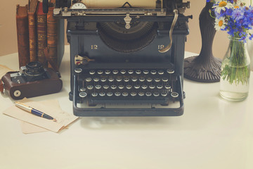 black vintage typewriter with books on white wooden table with copy space, retro toned