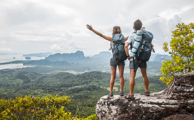 Hikers with backpacks relaxing on top of a mountain and enjoying the view of valley