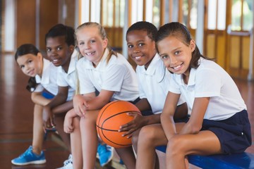 Portrait of school kids sitting in basketball court