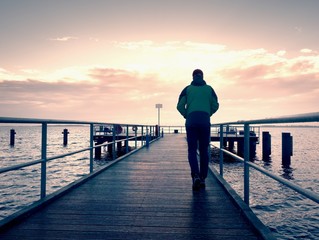 Tall man stand on mole wooden board and looking over ocean to Sun. Empty wharf,